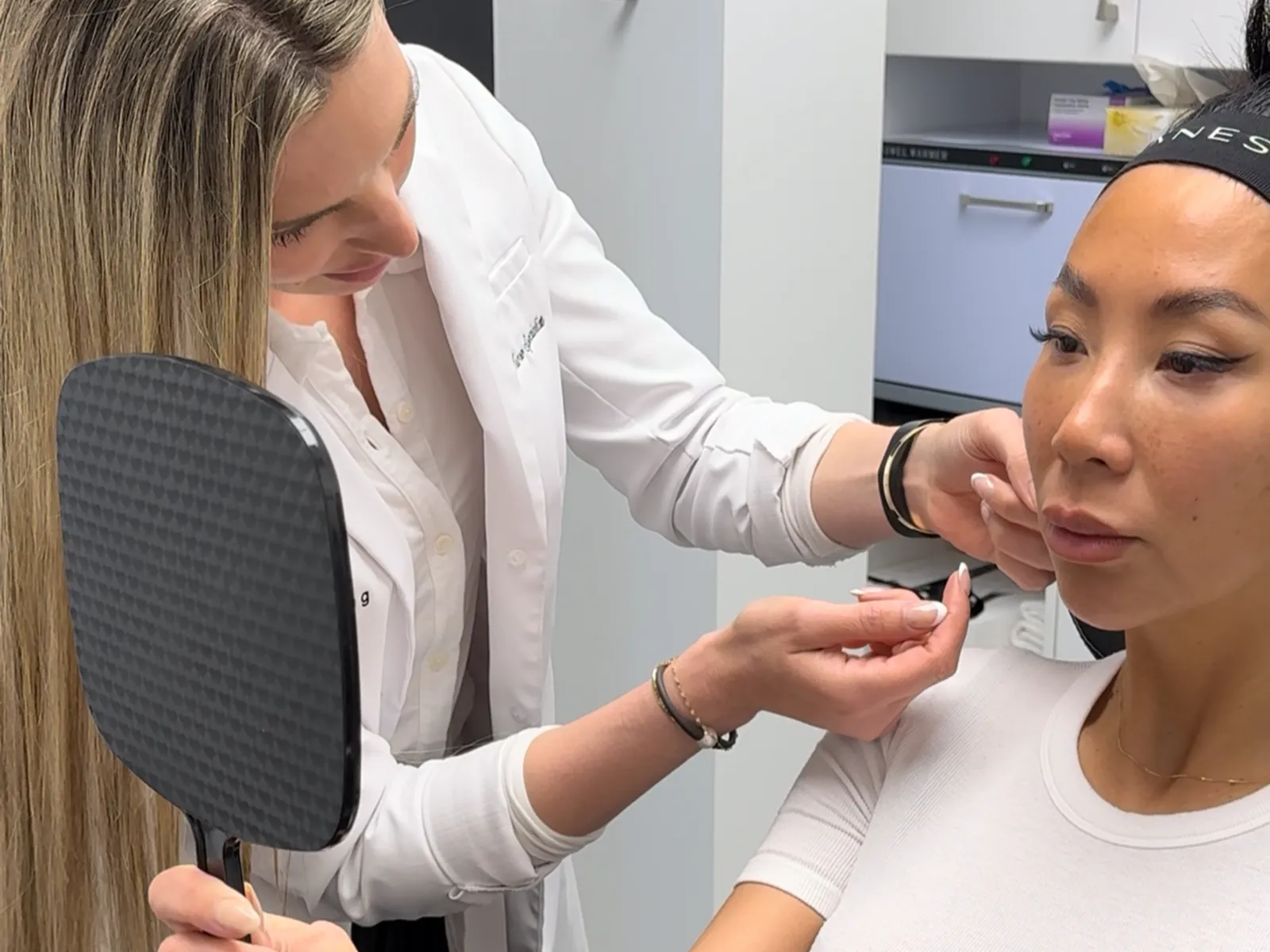 Sarita Hutton assessing a patient’s face during a skin rejuvenation consultation, the patient holding a mirror