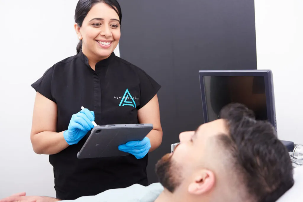 An Ageless Living practitioner charting beside a resting patient in a treatment room
